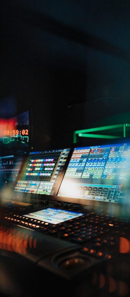 Theatre production lighting desk with computer screens and coloured lights. 